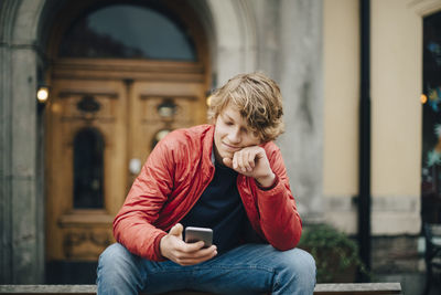 Teenage boy using mobile phone while sitting on bench in city