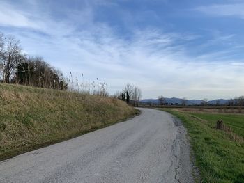 Empty road amidst field against sky