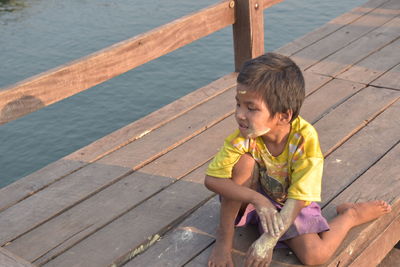 High angle view of boy sitting on wooden pier