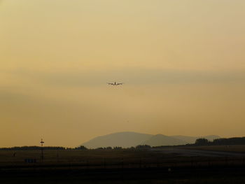 Airplane flying over runway against sky during sunset