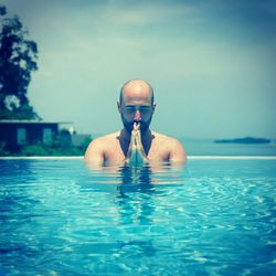 Portrait of shirtless man joining hands in swimming pool