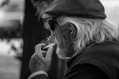 Side view of senior man smoking cigarette while sitting outdoors