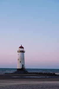 Lighthouse by sea against clear sky