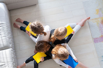 Four children sitting on floor leaning against each other in living room doing prep work for school