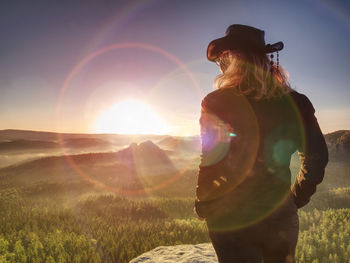 Cheering young woman traveler hiking on rocky mountain promontory above sharp tree tops.