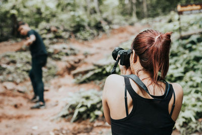 Rear view of young woman photographing man standing at forest
