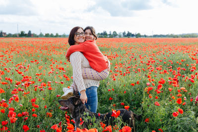 Standing in the field of poppies mother holding a daughter in arms and their dog next to them