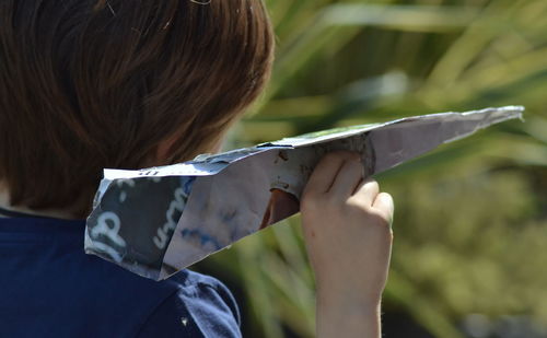 Rear view of boy holding paper airplane