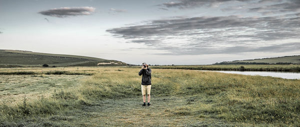 Full length of man photographing on grassy field