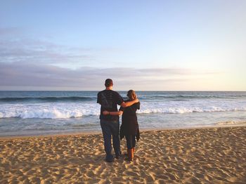 Rear view of couple standing on shore at beach during sunset