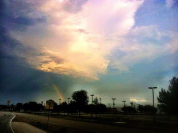 Road passing through field against cloudy sky