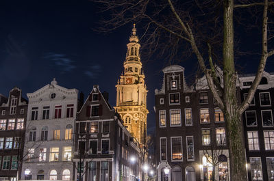 Low angle view of illuminated canal house and church tower at night in amsterdam 