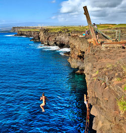 People on rock by sea against sky