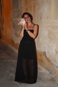 Portrait of woman holding seashell while standing against wall at night