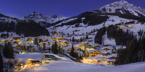 Snow covered trees by buildings against sky during winter at night