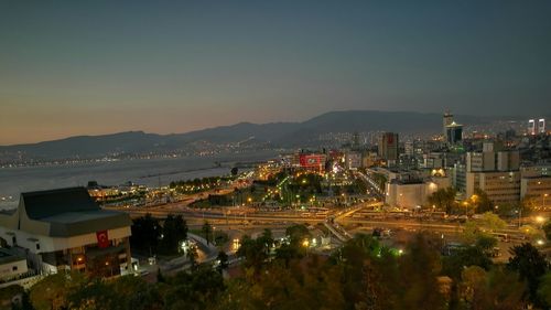 Illuminated city by river against clear sky