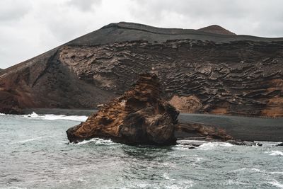 Rock formation in sea against cloudy sky