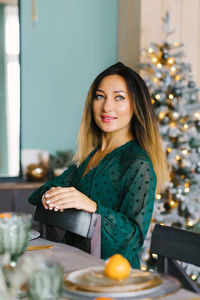 Portrait of a beautiful young woman in an emerald-colored dress stands near the christmas tree
