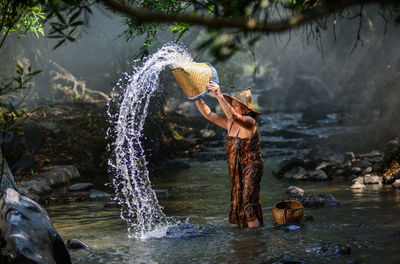 Senior woman splashing water in river at forest
