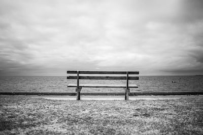 Empty bench on beach against sky