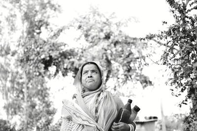 Low angle view of woman with bottles standing against trees