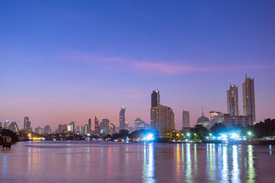 Illuminated buildings by river against sky in city