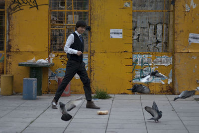 Full length of smiling man walking on footpath by pigeons