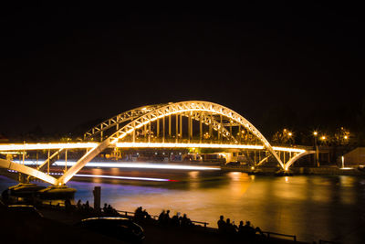 Illuminated bridge over river against sky at night