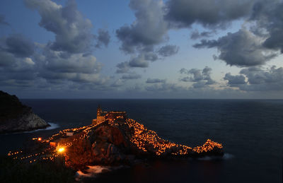 Illuminated city by sea against sky at night