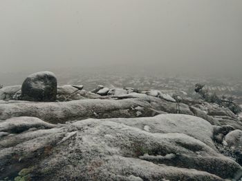 Scenic view of snowed rocks against foggy day during winter