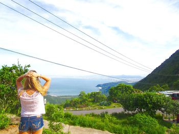 Rear view of woman with hand in hair looking at mountain against sky