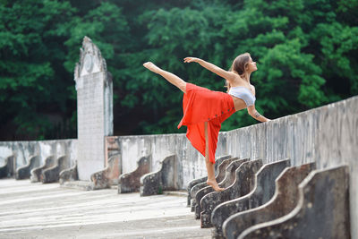 Young woman dancing while standing by retaining wall