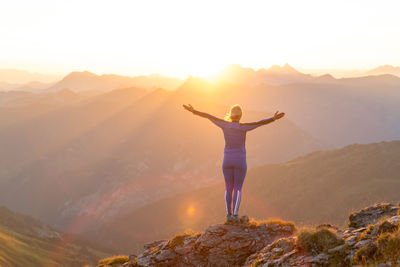 Rear view of woman standing on mountain peak against sky during sunrise