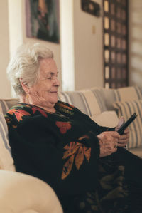 Focused senior female with gray hair resting on couch and reading e book on tablet in living room at home
