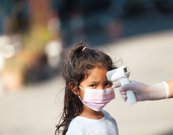 Cropped hand checking temperature of cute girl outdoors