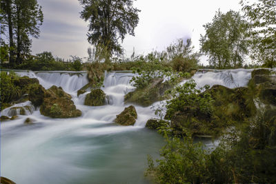 Scenic view of waterfall in forest against sky