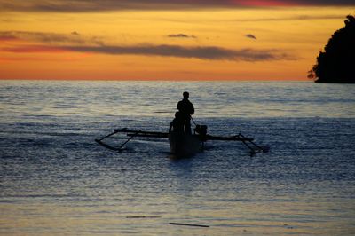 Silhouette man sitting in sea against sky during sunset