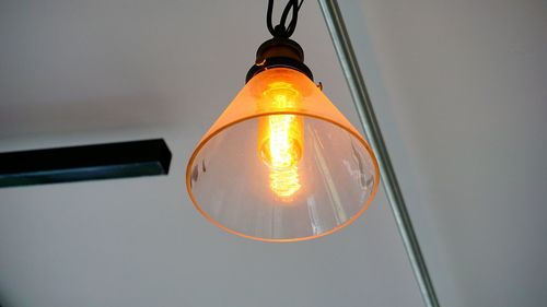 Low angle view of illuminated light bulb hanging against sky