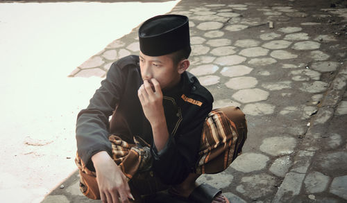 Young man looking away while sitting on wall