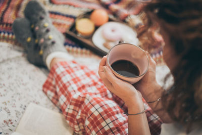 High angle view of woman holding coffee cup on bed