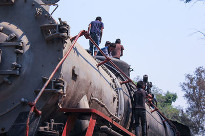Low angle view of boys climbing freight train against clear sky