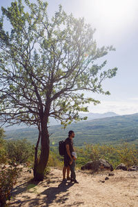 Father with a backpack and his son stands next to a tree on a mountain in the summer in the crimea