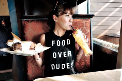 Woman drinking drink while holding plate with cake at restaurant