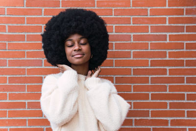 Portrait of young woman standing against brick wall