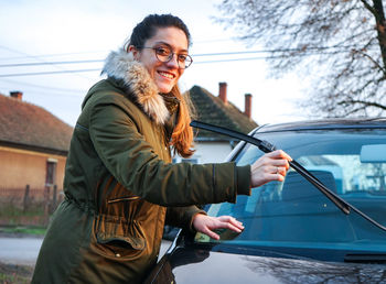 Portrait of smiling young woman holding windshield wiper in town