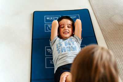 High angle positive little boy in sportswear with hands behind head doing sit ups on yoga mat