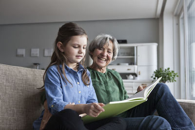 Grandmother and her granddaughter sitting together on the couch with a book