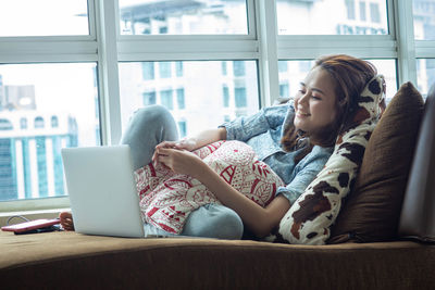 Midsection of woman using mobile phone while sitting on window