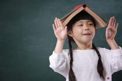 Girl with book on head standing by blackboard