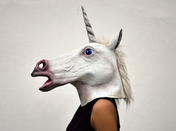 Side view of woman wearing horse mask against white background